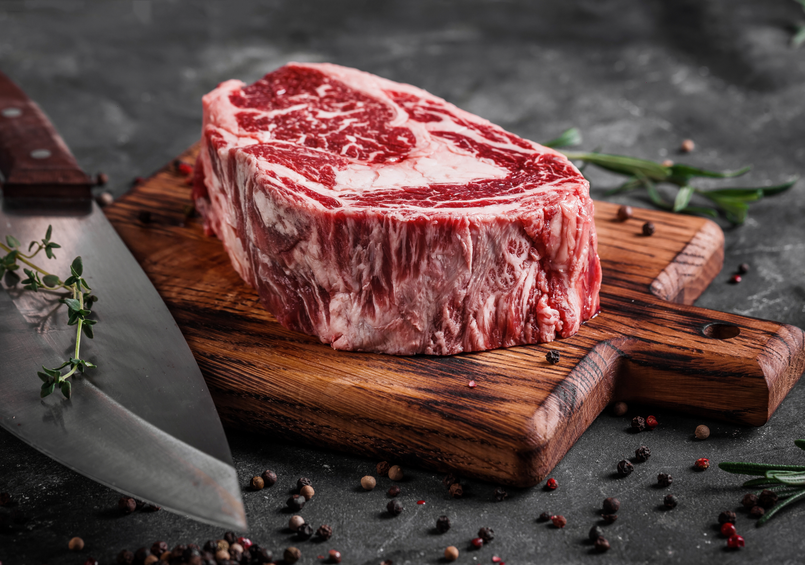 A guy in a leather apron is slicing raw meat. The butcher cuts the pork ribs. Meat with bone on a wooden cutting board.